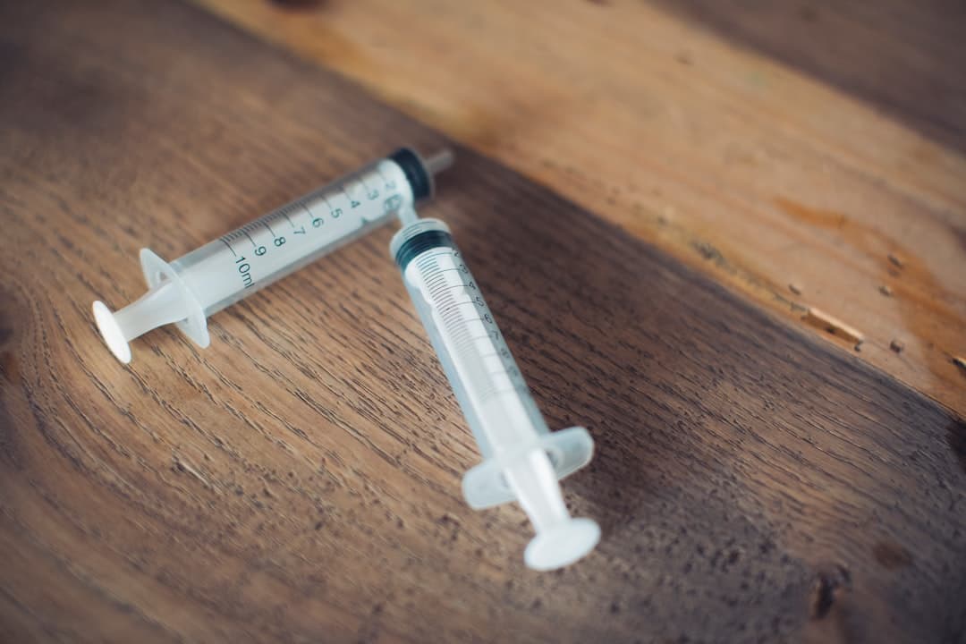 A white and black plastic syringe resting on a brown wooden table.