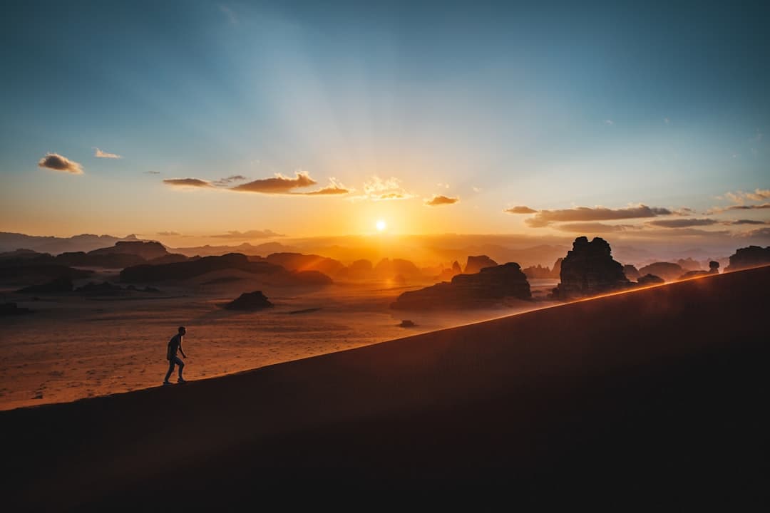 A figure silhouetted against sunrise on a sandy hill