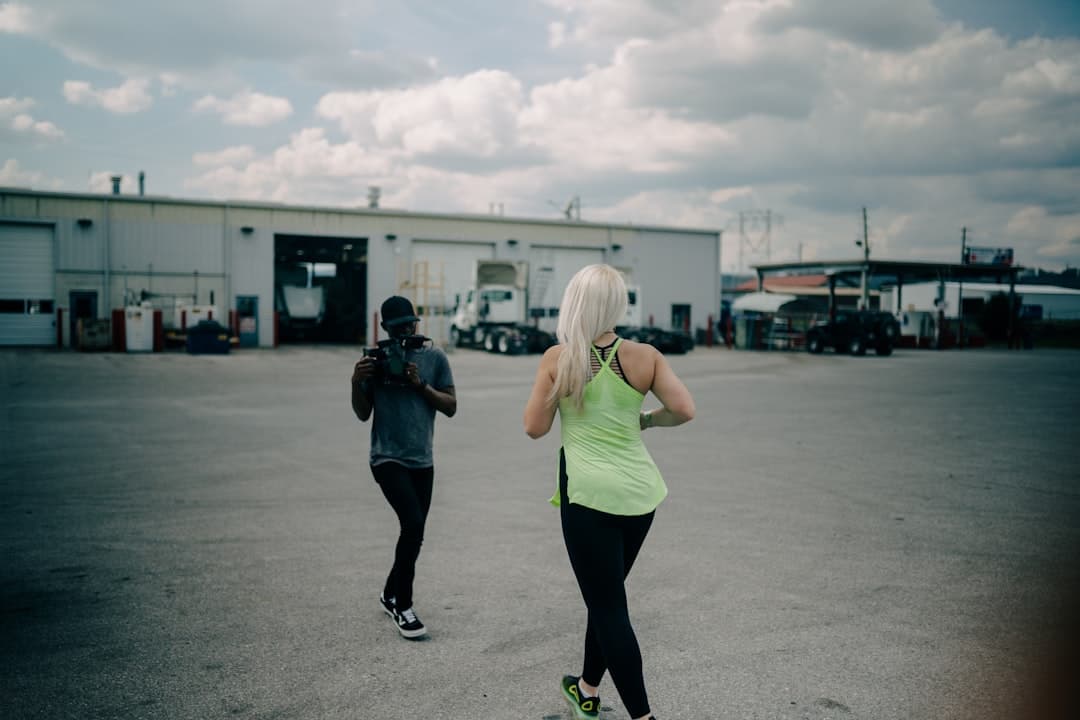 A woman in a green tank top and black leggings standing on a road during the day.