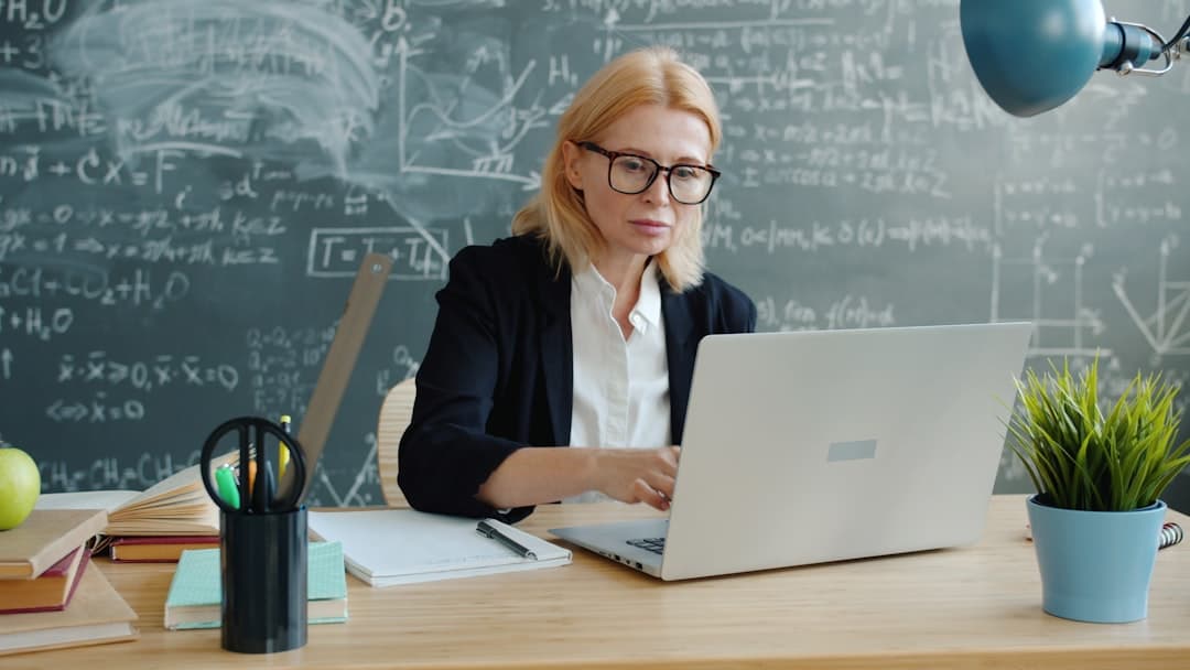 A woman working on a laptop in front of a chalkboard.