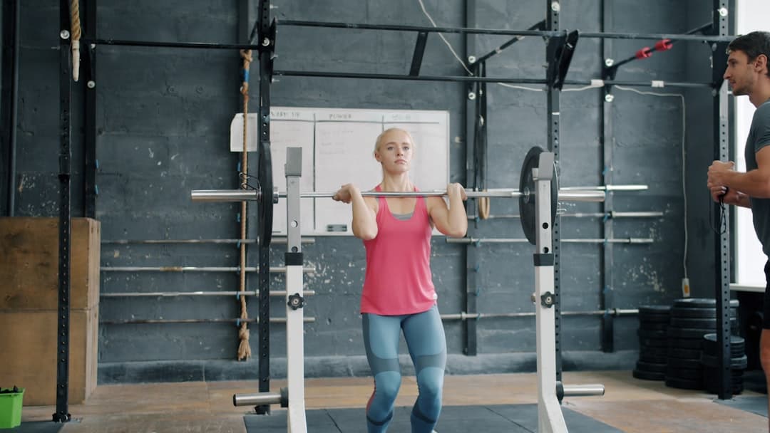 A lifter performing a barbell exercise with a trainer watching.
