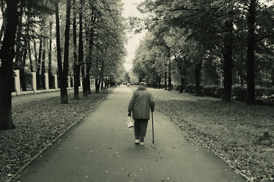 An elderly person walking on a park path with a cane